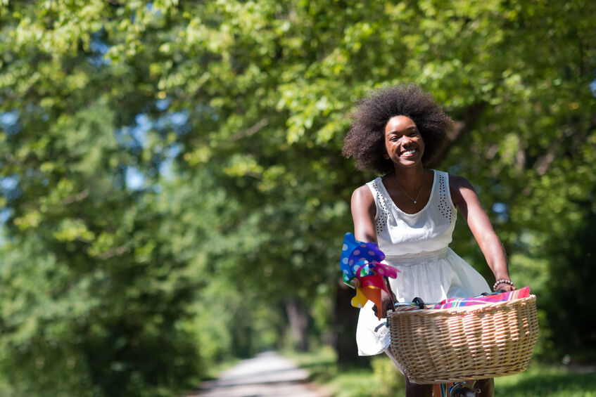 Young woman riding her bike in a white dress managing her period symptoms during the summer.