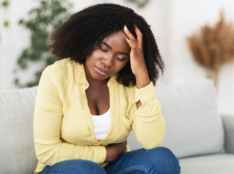 Sad black woman suffering from PMS and menstruation pain. Having stomach ache, abdominal pain and headache