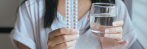 Close up of hand female holding birth control pill and a glass of water