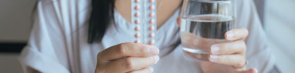 Close up of hand female holding birth control pill and a glass of water