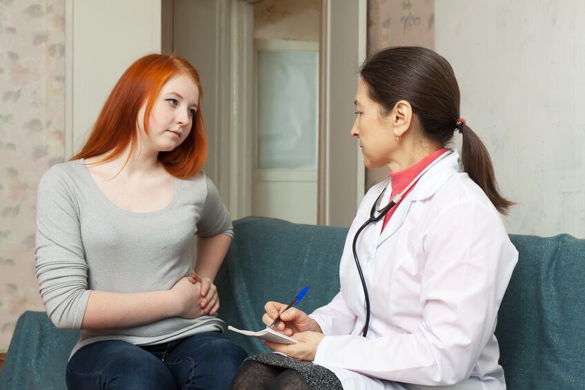 sick young girl complaining to doctor about stitch in side at home