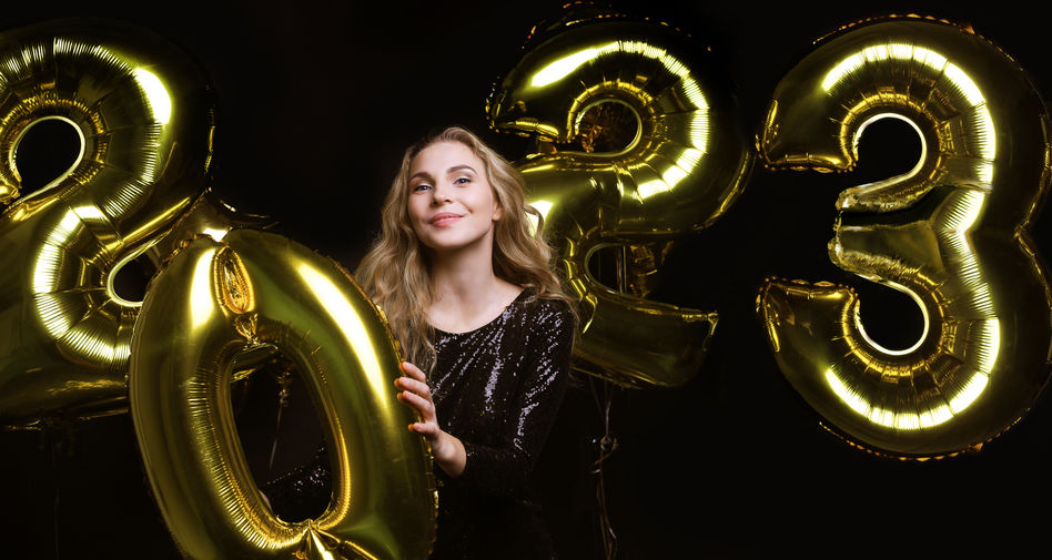 Happy gorgeous girl in stylish sexy party dress holding gold 2023 balloons, having fun at New Year's Eve Party